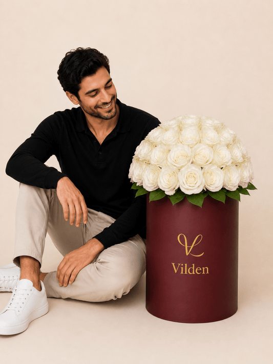 Male model with luxury pearl phere white roses in a burgundy Vilden flower box on a beige studio background.