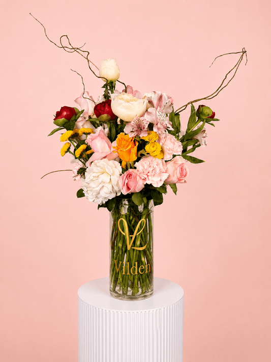 Garden Sonata with pink roses, white blooms, yellow flowers, and carnations in a clear Vilden vase.