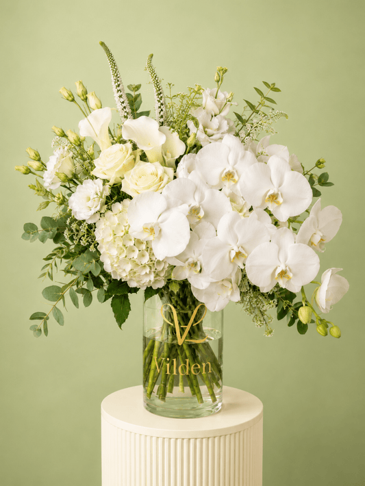 Luxury White Opera arrangement with cream roses, white calla lilies, hydrangea, and fresh greenery in a clear Vilden vase.
