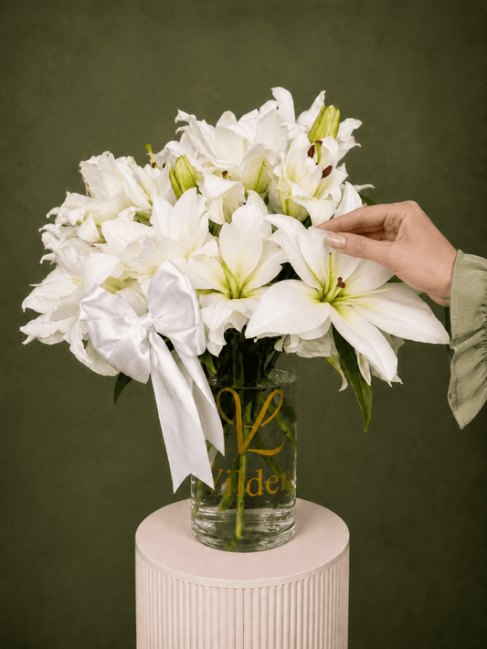 Ivory Lily Reverie with white lilies, unopened lily buds, and a white satin bow in a clear Vilden vase with a soft tough