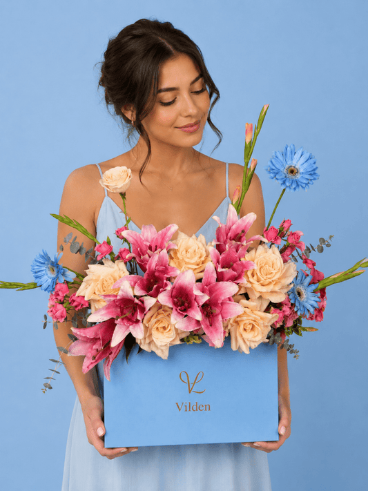 Female model holds the Petal Sky Vilden flower box with pink lilies, cream roses, and blue blooms.