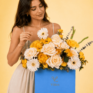 Female model with blue Vilden flower box of yellow roses and white blooms on cream stand.