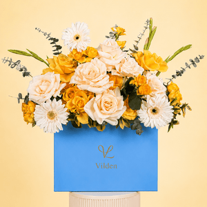 Golden harmony flower arrangement in a blue box with ivory roses, yellow roses, white gerbera daisies, and eucalyptus.