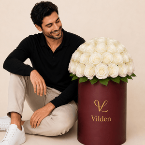 Male model with luxury pearl phere white roses in a burgundy Vilden flower box on a beige studio background.