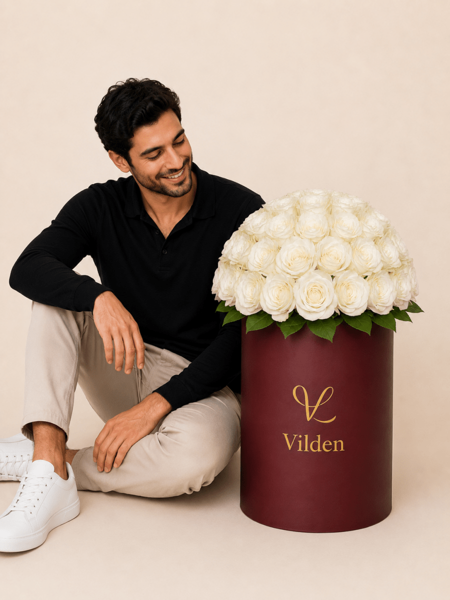 Male model with luxury pearl phere white roses in a burgundy Vilden flower box on a beige studio background.