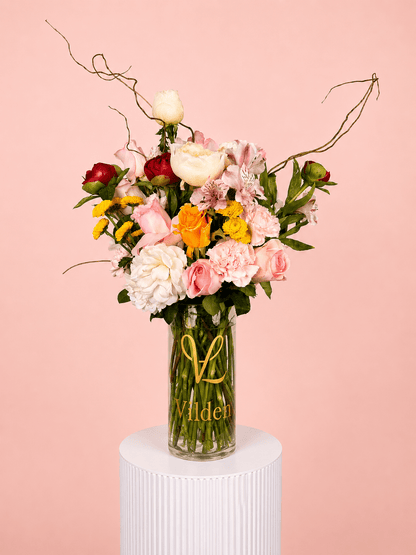 Garden Sonata with pink roses, white blooms, yellow flowers, and carnations in a clear Vilden vase.