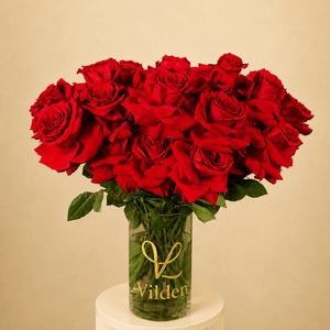 Vilden Rouge arrangement in a clear Vilden vase on a creamy white ribbed pedestal against a soft warm beige background.