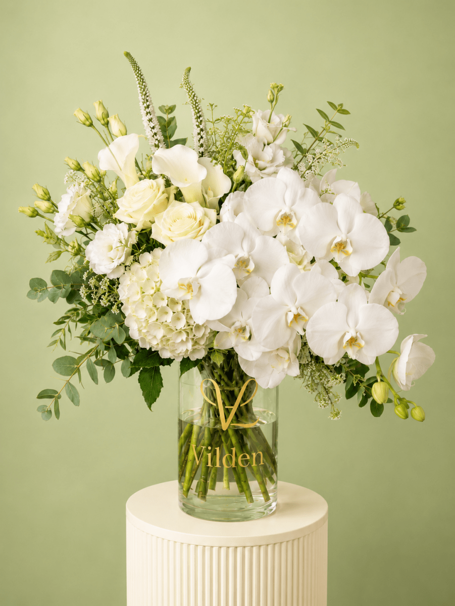 Luxury White Opera arrangement with cream roses, white calla lilies, hydrangea, and fresh greenery in a clear Vilden vase.
