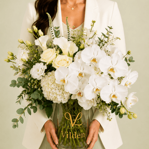 A person holding a luxury White Opera arrangement with cream roses, white calla lilies, hydrangea in a clear Vilden vase.